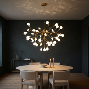 Bion brass 45-light sputnik chandelier lit above an oval travertine dining table against a deep charcoal-green wall