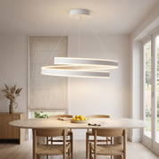 Andromache ringed Nordic LED chandelier in matte white lit above an oval travertine dining table in a bright airy dining room