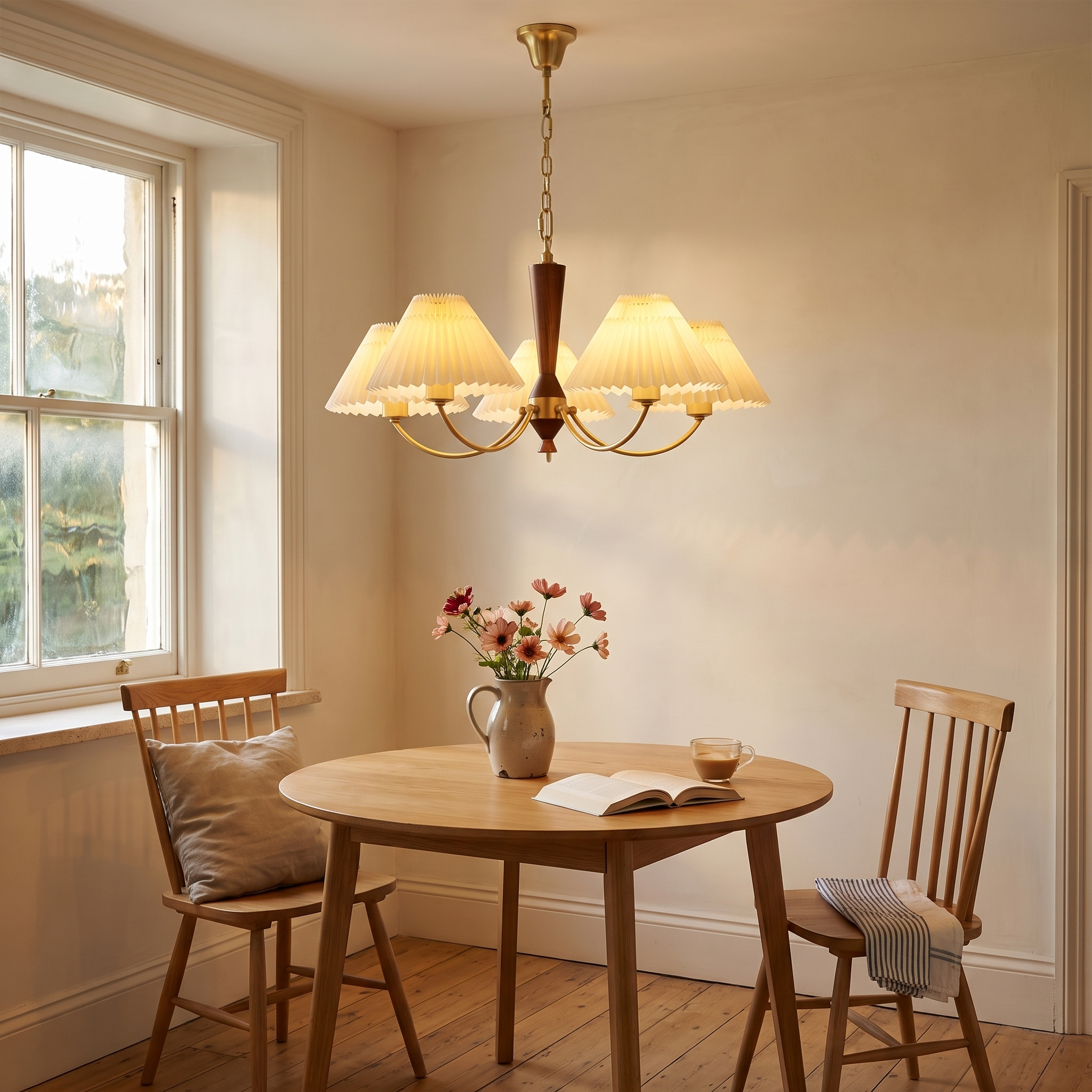 Baukis pleated shade copper and walnut chandelier lit above a round oak breakfast table in a warm limewash kitchen dining nook