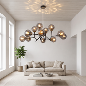 Deiphobos twelve-globe glass chandelier lit in a bright airy white living room with oatmeal linen sofa and travertine table