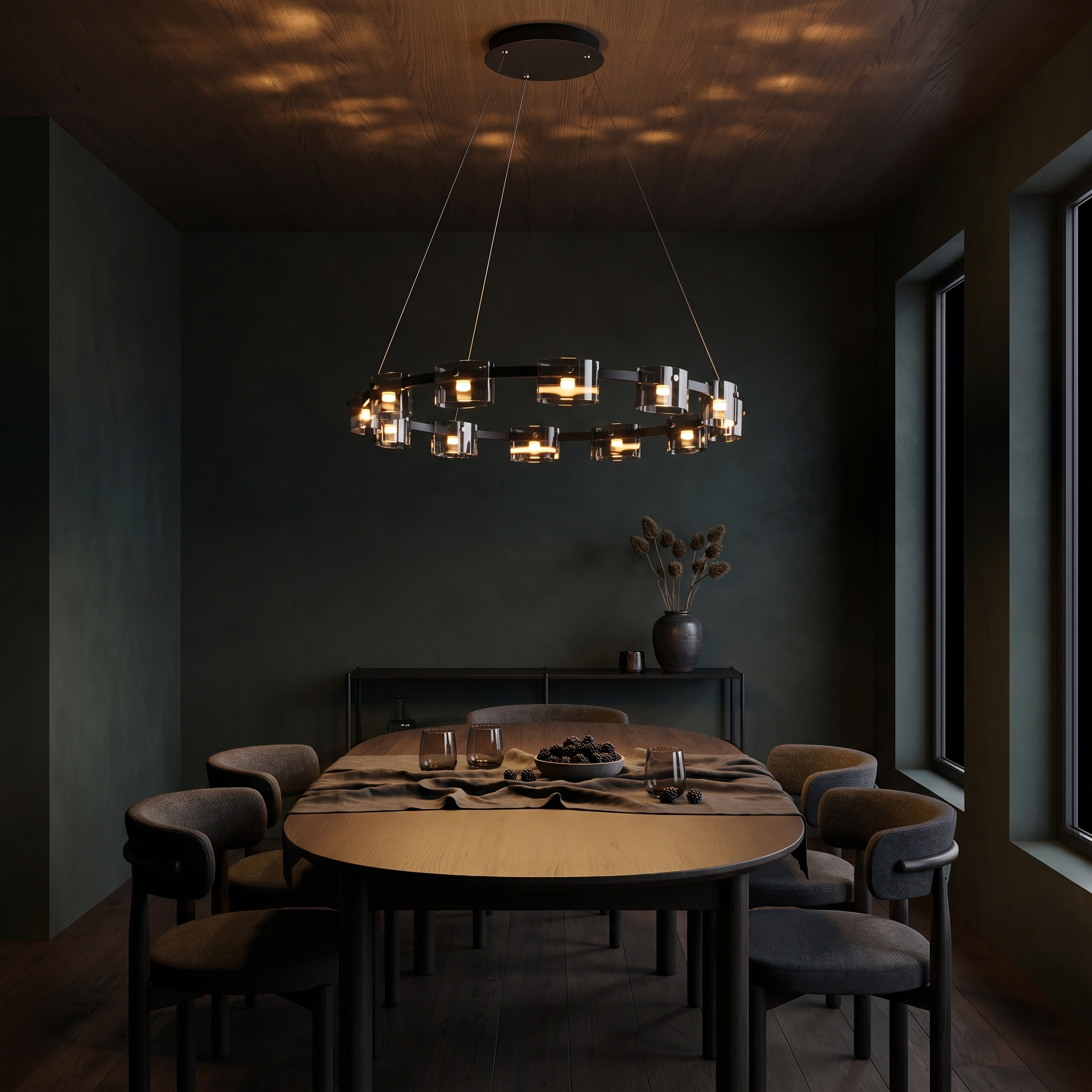 Diokles circle glass chandelier lit over a dining table in a dark inky green dining room at night