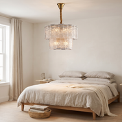 Eirene brass and textured glass tiered chandelier lit in a bright plaster and oak bedroom with linen bedding