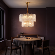 Eirene brass and textured glass tiered chandelier lit over a round table in a dark aubergine dining room at night