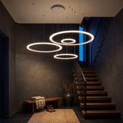 Amyntas four ring LED chandelier in white cascading through a dark charcoal double-height stairwell at dusk