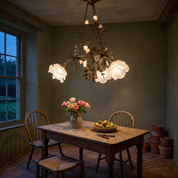 Erato brass and glass flower chandelier lit above a scrubbed oak table in a dark sage green garden room