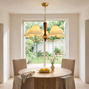 Baukis five-light brass and walnut pleated-shade chandelier above a travertine table in a bright garden room