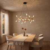 Elpis twenty-light gold crossed-baton chandelier lit over an oak dining table in a warm sand plaster room at dusk