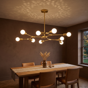 Berenika nine-light gold branching sputnik chandelier with opal globes lit over an oak table in a warm clay dining room