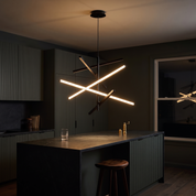 Nikandros Nordic Linear Chandelier glowing over a soapstone island in a dark charcoal-green evening kitchen