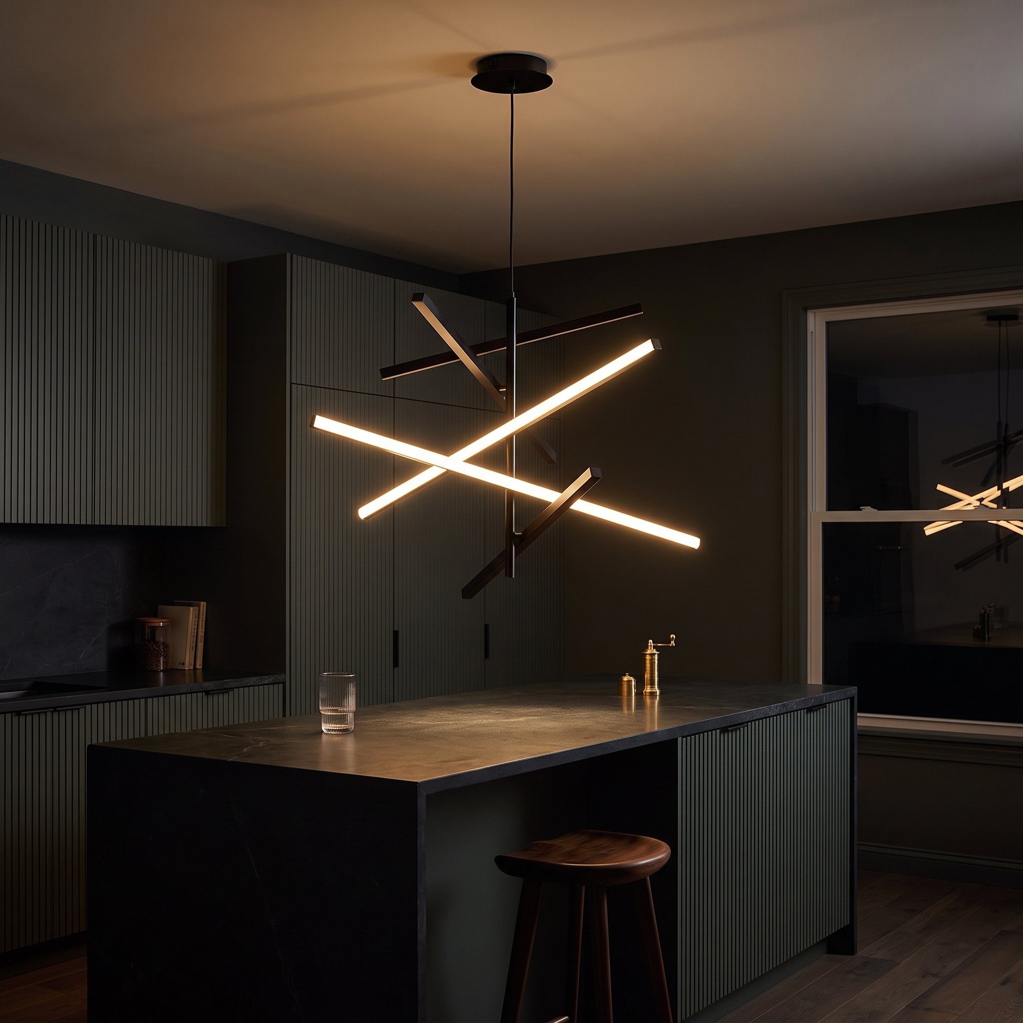 Nikandros Nordic Linear Chandelier glowing over a soapstone island in a dark charcoal-green evening kitchen
