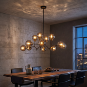 Deiphobos Twelve-Globe Glass Chandelier lit above a walnut table in a dark concrete dining room