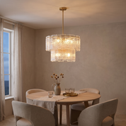 Eirene Brass and Glass Tiered Chandelier lit above a round oak table in a warm plaster dining room