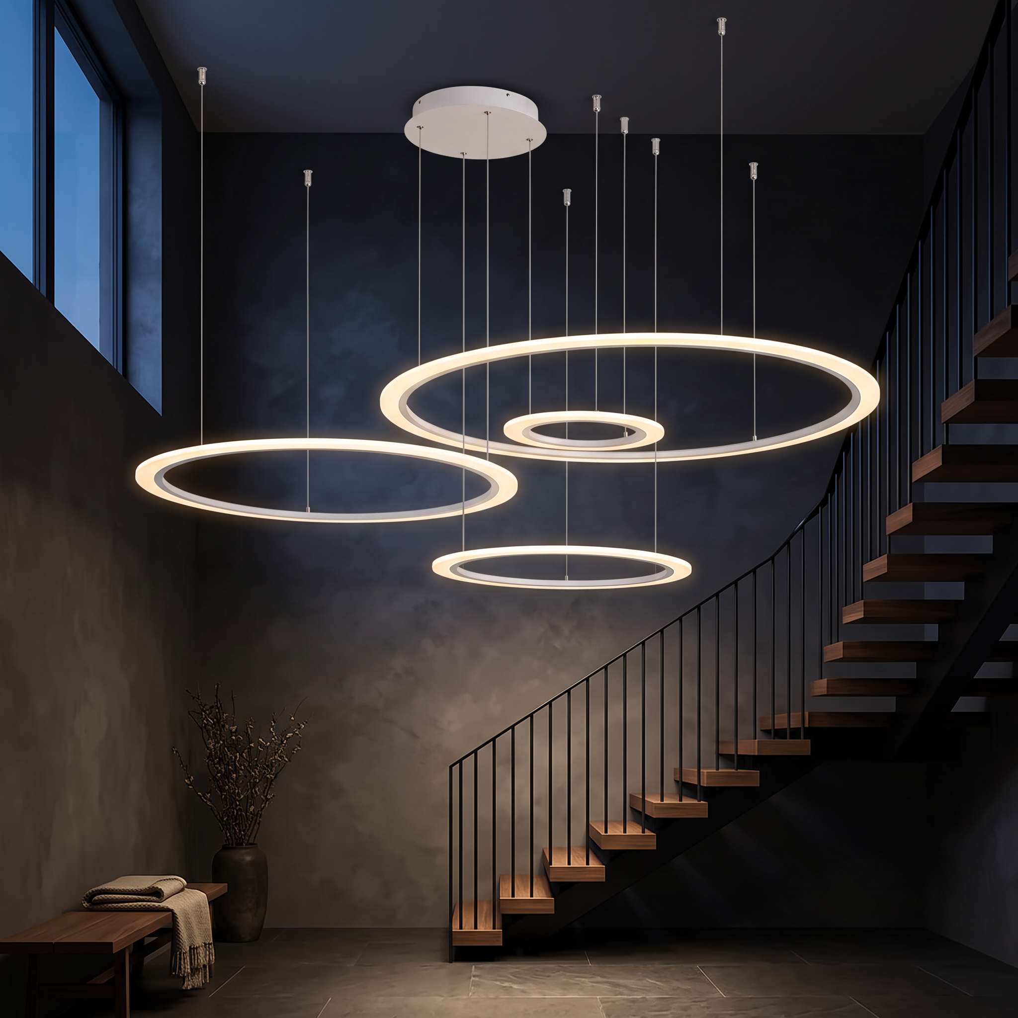 Amyntas Four Ring Artistic LED Chandelier glowing in a dark double-height stairwell with walnut treads