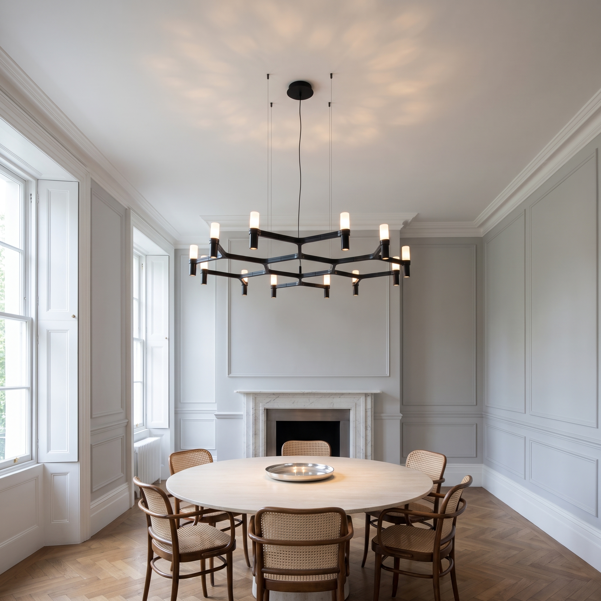 Euthymios geometric layered Nordic chandelier lit above a round table in a bright dove-grey panelled morning room