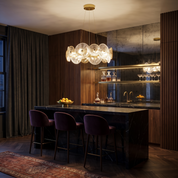 Bakchylides brass frame glass chandelier lit above a black marble counter in a dark walnut home bar
