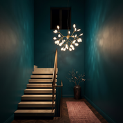 Chryseis 36-light gold sputnik chandelier lit in a deep teal stairwell with a cantilevered stone stair at night