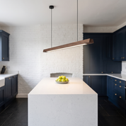 Alkinoos linear wood chandelier over a quartz island in a navy painted-brick kitchen